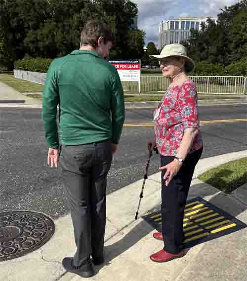Beezy and a man are standing in a curb ramp near one of the tactile alignment pads.